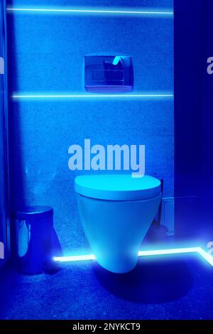 Toilet bowl in public restroom lit with UV blue light Stock Photo