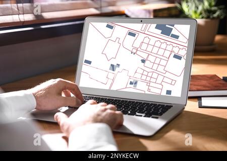 Man analyzing cadastral map on laptop at table, closeup Stock Photo