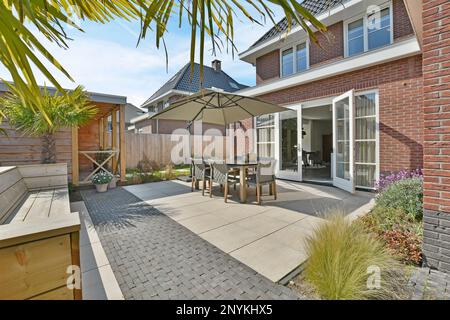 Amsterdam, Netherlands - 10 April, 2021: a patio with an umbrella over the table and some plants on the side of the house in the back yard Stock Photo