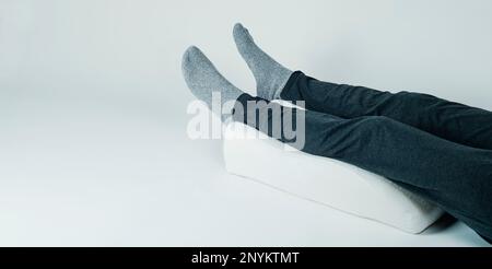 closeup of a man using a leg elevation pillow, made of memory foam, laying on a white background, in a panoramic format to use as web banner Stock Photo