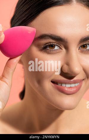 close up view of happy woman holding makeup sponge isolated on pink,stock image Stock Photo