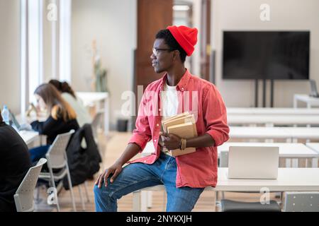 Black student guy looking out of window thinking about weekend plans while studying in library Stock Photo