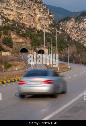 Car with motion blur driving on highway towards tunnel under hill. Stock Photo