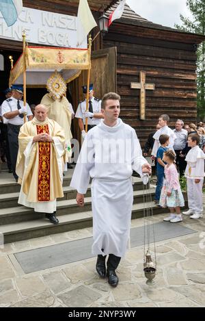 Altar server with incense, local priests holding a monstrance, firefighters carrying a baldachin, leaving wooden church, Corpus Christi celebration in Letownia, Gorals (Polish highlander people) village, Beskids mountain range, Western Carpathians, Malopolska region, Poland Stock Photo