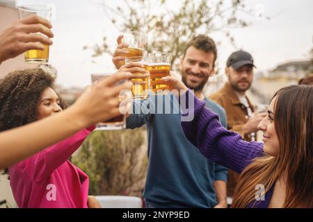 Multietnic student friends toast beers on hostel terrace celebrating end-of-year party - people lifestyle concept Stock Photo
