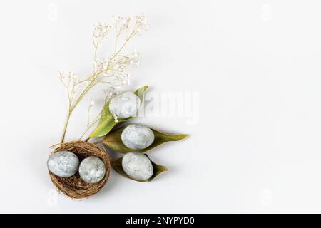 Minimal ecological Easter concept with dried flowers. Gray eggs on dry magnolia leaves and in a brown nest of twigs on a gray background Stock Photo