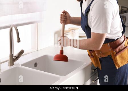 Plumber using plunger to unclog sink drain in kitchen, closeup Stock Photo