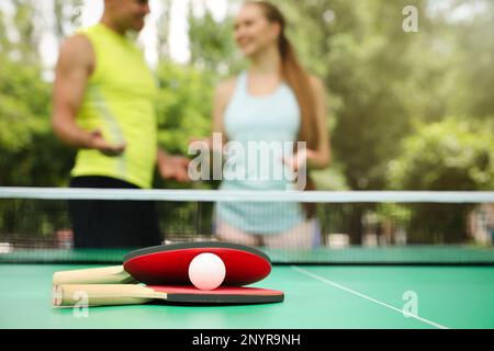 Couple talking near ping pong in park, focus on rackets and ball Stock Photo