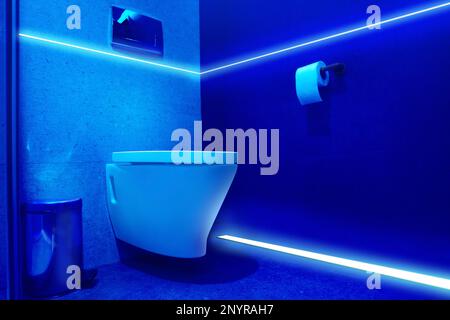 Toilet bowl in public restroom lit with UV blue light Stock Photo