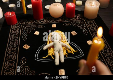 Voodoo doll pierced with pins and woman holding candle above black mat, closeup. Curse ceremony Stock Photo