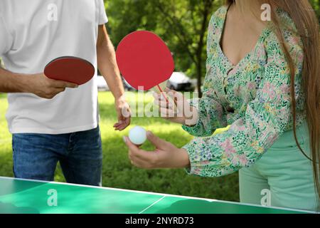 Couple with tennis rackets and ball near ping pong table in park, closeup Stock Photo