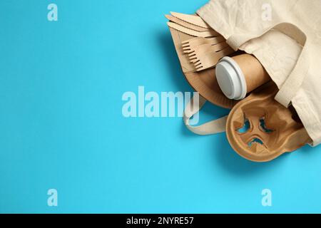 Flat lay of paper and wooden tableware in cotton bag on turquoise background, space for text. Eco friendly lifestyle Stock Photo