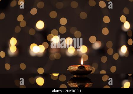 Lit diya on table against blurred lights, space for text. Diwali lamp Stock Photo