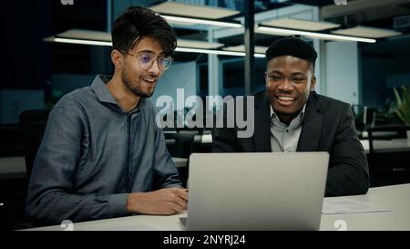 Male african indian colleagues workers men happy business people businessman laughing looking at computer screen having fun humor talking joke laugh Stock Photo