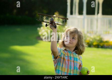 Kid having fun with toy airplane in field. Child pilot aviator with airplane dreams of traveling in summer in nature Stock Photo