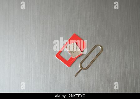 a sim card and a paper clip for opening a slot for a sim card lies on a gray steel background Stock Photo