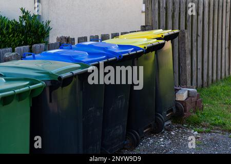 Plastic large trash cans with the lids up and garbage inside against a  brick orange wall. Big green and grey plastic dumpsters on a city street.  Waste Stock Photo - Alamy