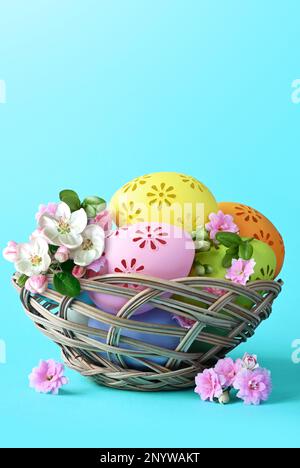Multi colors Easter eggs in the basket and flowers on blue background. Pastel color Easter eggs Stock Photo