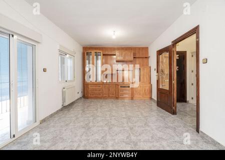 Empty living room with gray stoneware floors, dark wood access doors with glass, custom made bookcase with wood paneling on one wall and access to a t Stock Photo