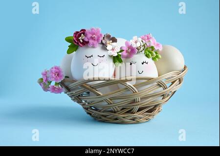 Natural eggs with drawn smiling face in cute floral crown on blue background. Happy Easter. Stock Photo