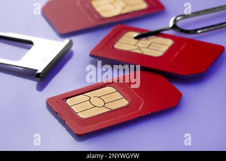 SIM cards, tray and ejector on violet background, closeup Stock Photo