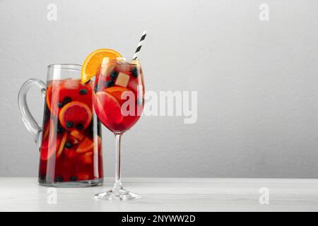 Glass and jug of Red Sangria on white wooden table against light grey background. Space for text Stock Photo