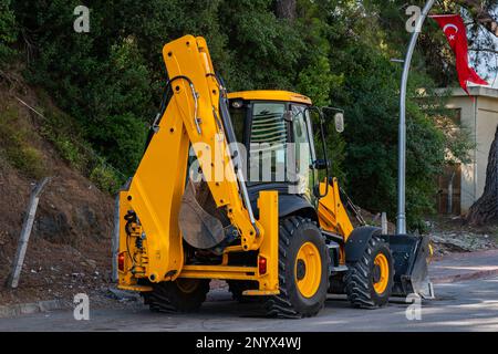 Yellow wheeled excavator standing on the side of the road. The Turkish flag flies on a pole. Stock Photo