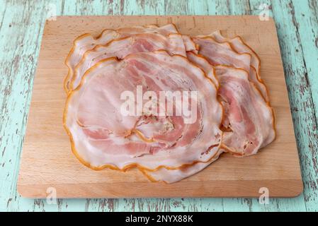 Porchetta, roast pork slices on cut out wooden cutting board on turquoise colored wooden board, with clipping path Stock Photo