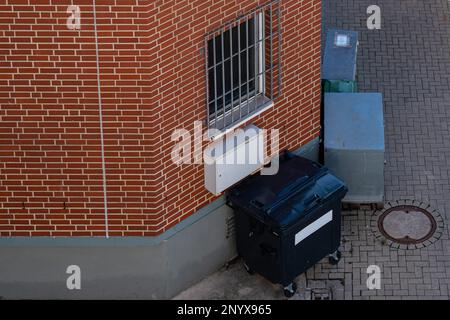 Black garbage container standing near the wall of the house. View from above. Stock Photo