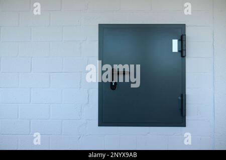 Gray metal door in a white brick wall. Close up. Stock Photo