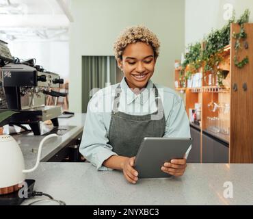 Young smiling barista holding a digital tablet at bar counter. Female entrepreneur in an apron with digital tablet in her cafe. Stock Photo