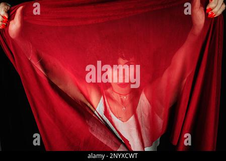 Portrait of a woman with red cloth stretched in front of her face. isolated on black background. Stock Photo