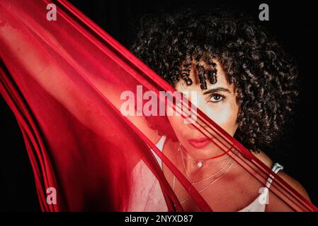 Portrait of a woman with red cloth stretched in front of her face. isolated on black background. Stock Photo