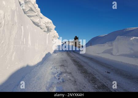 Snowbanks tower over a road in Mammoth Lakes, CA after storms dumped over 10 feet of snow on the Sierra Nevada town. Stock Photo