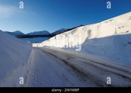 Snowbanks tower over a road in Mammoth Lakes, CA after storms dumped over 10 feet of snow on the Sierra Nevada town. Stock Photo