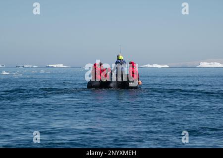Inflatable boat full of tourists cruises among icebergs in Antarctica
