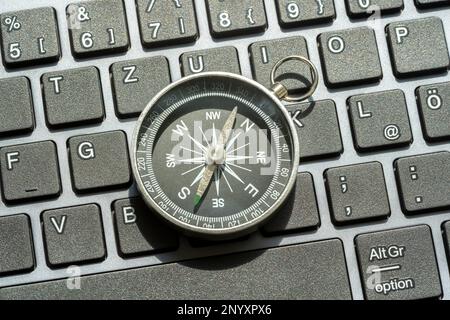 One single compass laying on a modern computer desktop PC keyboard, world navigation, different directions, NSWE object closeup, nobody, central compo Stock Photo