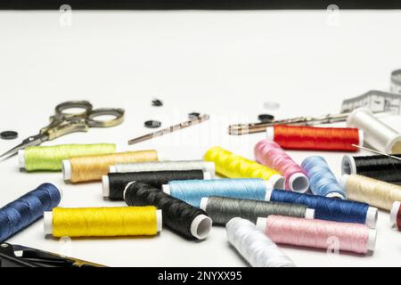 Still life with various coils of colored thread on a white surface, scissors, buttons and other accessories Stock Photo