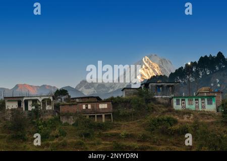 Snow capped mountain peak of Choukhamba range with tourist bungalows and resorts at Deoriatal, Uttarakhand, India. Sun set light on snow peaks. India. Stock Photo