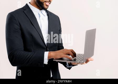 Cropped photo of bearded african-american freelancer guy using laptop computer isolated on white background, dark-haired 30s multiracial man in formal black suit typing, face is not visible Stock Photo
