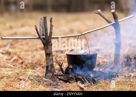 A cauldron with a lid hangs over the fire on wooden slingshots and a crossbar. Stock Photo