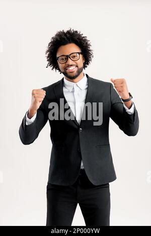 Goal achievement concept. Excited businessman in suit looking at the camera and rejoicing with good news or successful deal. Emotional lucky man with wide smile raising fists up, triumph and victory Stock Photo