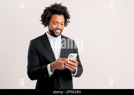 Happy businessman in formal office wear using smartphone isolated on white, african-american guy chatting online, using new mobile app, testing, web surfing Stock Photo