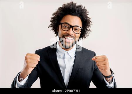 Extremely excited overjoyed african-american man with curly hair shouting making yes gesture, amazed with his victory, triumph, looking at camera and laughing, studio shot isolated on white background Stock Photo