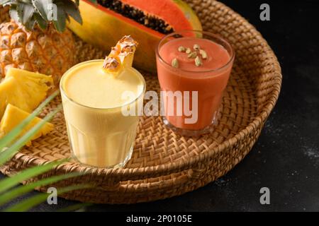 Pineapple and papaya lassie or smoothie in tray on black background. Traditional Asian beverage of pineapple, papaya and ice. Close up. Stock Photo