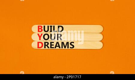 BYD build your dreams symbol. Concept words BYD build your dreams on wooden stick on a beautiful orange table orange background. Business and BYD buil Stock Photo