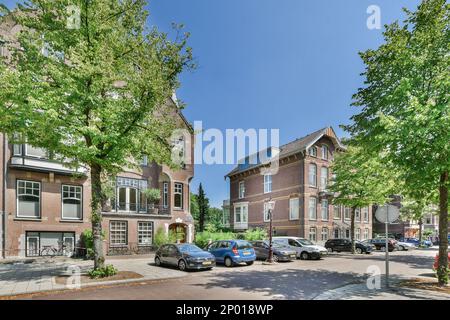 Amsterdam, Netherlands - 10 April, 2021: a city street with cars parked on the side and trees lining the street in front of buildings, all lined up against each other Stock Photo
