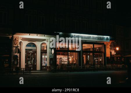 A restaurant is shown from the outside at night. Inside the lights are burning and outside there are chairs. The restaurant is located in a Germany. Stock Photo