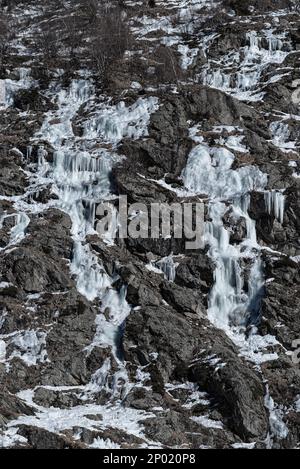 Several frozen water streams forming ice flows and icicles on a dry rocky mountainside in winter in Chamonix, France Stock Photo