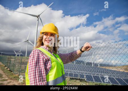 An engineer checks her smart watch while at the solar power plant Stock Photo